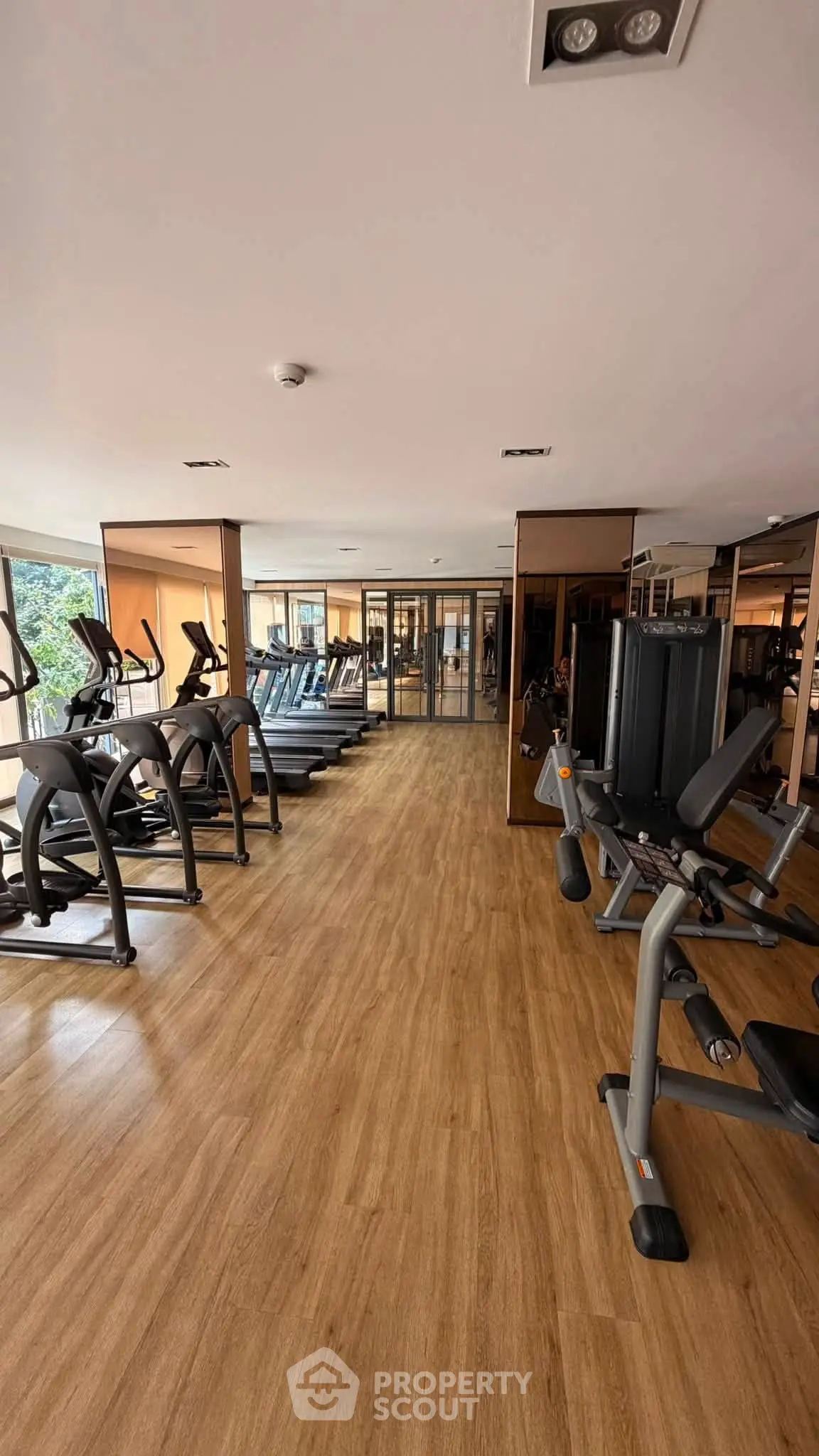 Spacious gym with modern fitness equipment and wooden flooring in a residential building.