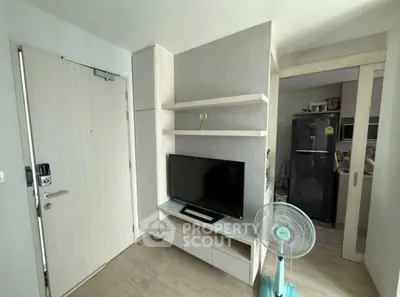 Modern apartment interior with TV, shelves, and kitchen view, showcasing compact living space.