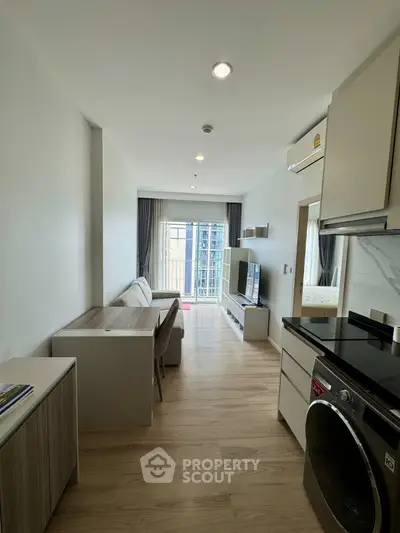 Modern apartment interior with open layout, featuring sleek kitchen and cozy living area with balcony view.