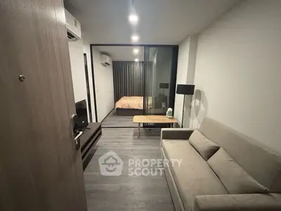 Modern apartment with open layout, featuring cozy living room and bedroom separated by glass partition.