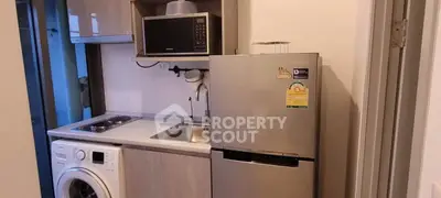 Compact kitchen with modern appliances including fridge, microwave, and washing machine in a cozy apartment.