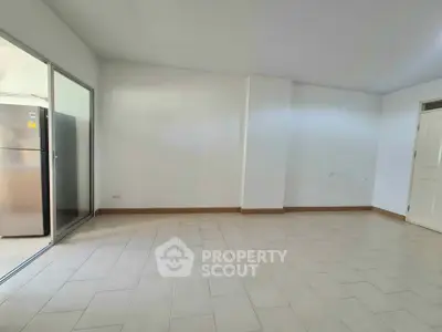 Spacious unfurnished living room with tiled flooring and sliding glass door to kitchen area.