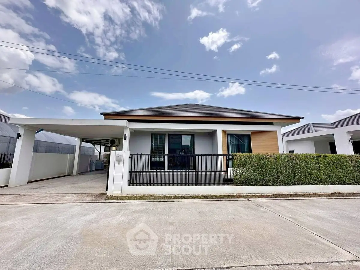 Modern single-story house with driveway and manicured hedge under blue sky.