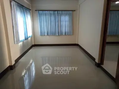 Spacious and well-lit empty room with glossy tiled flooring, large windows with sheer curtains, and a neutral color scheme awaiting personalization.