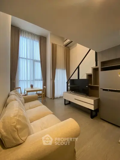 Modern living room with high ceilings and large windows, featuring a cozy beige sofa and sleek entertainment unit.
