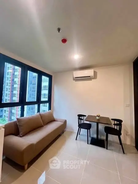 Modern living room with large windows and cozy furniture in a high-rise apartment.