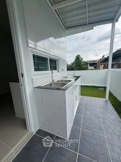 Modern outdoor kitchen with sleek stainless steel sink and tiled flooring, perfect for entertaining.