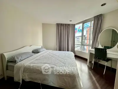 Spacious bedroom with large window and modern furnishings in a city apartment.
