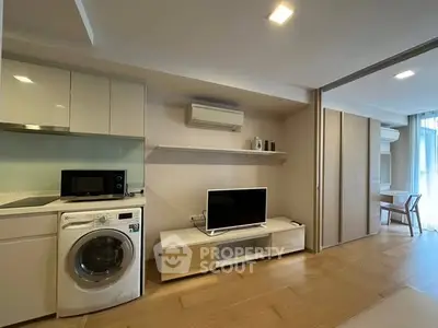 Modern living room with integrated kitchen featuring washing machine and TV setup.