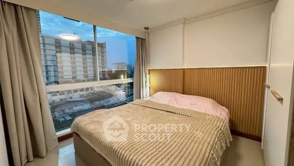 Cozy bedroom with large window offering city view, featuring modern decor and soft lighting.