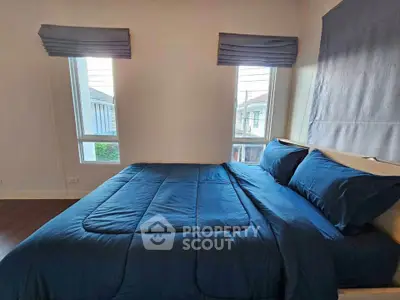 Cozy bedroom with blue bedding and natural light from two windows, perfect for relaxation.