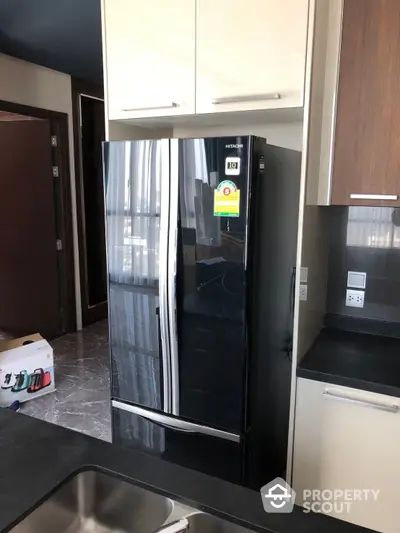 Modern kitchen with sleek black refrigerator, ample cabinetry, and built-in stainless steel sink, showcasing a blend of functionality and style.