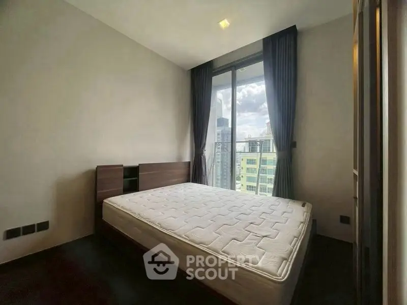 Spacious bedroom with large window offering city view, featuring a comfortable bed and modern design.
