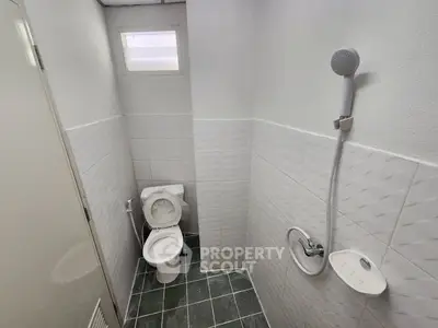 Compact bathroom with toilet and shower, tiled walls and floor.