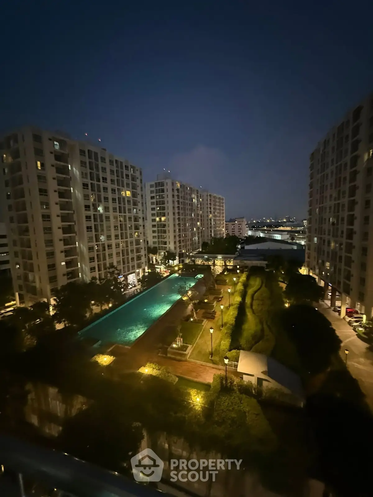 Stunning night view of modern apartment complex with illuminated pool and lush gardens.