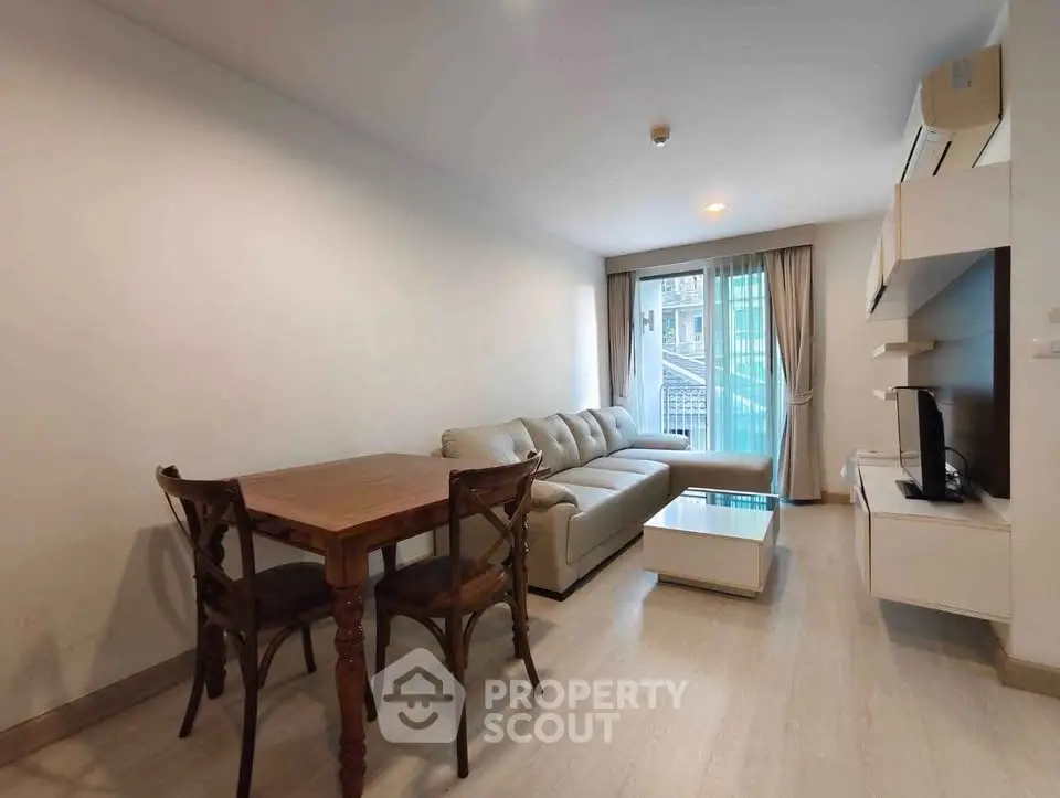 Modern living room with cozy sofa, dining table, and large window offering natural light.