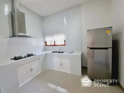 Modern kitchen with gas stove and stainless steel fridge in a bright, tiled space.