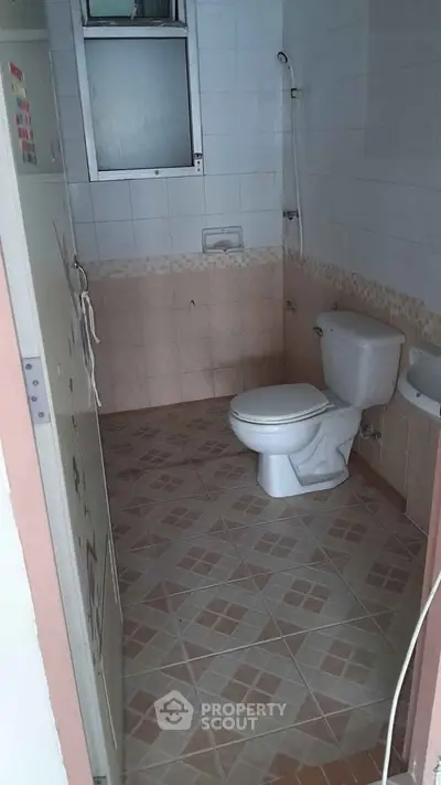 Compact bathroom with tiled floor and wall, featuring a toilet and small window.