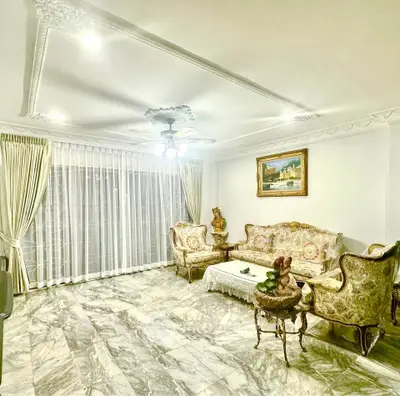 Elegant living room with marble flooring and vintage furniture, featuring ornate ceiling details and large window.