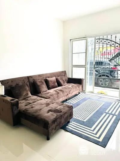 Spacious living room with plush brown sofa and modern rug, featuring natural light from large windows.