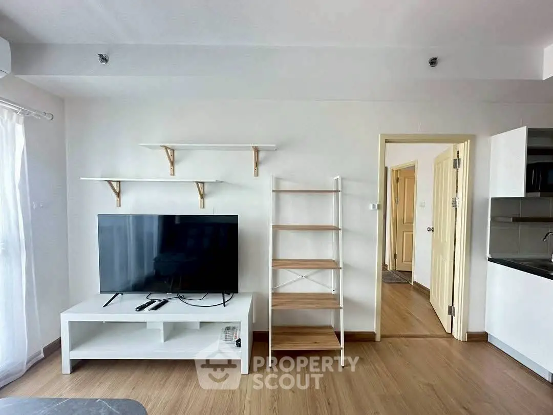 Modern living room with TV, shelves, and open kitchen layout in a bright apartment.
