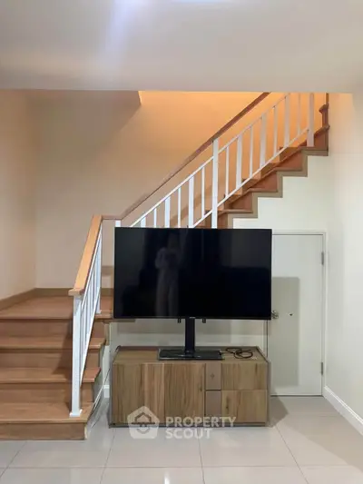Modern living room with sleek staircase and large TV, perfect for stylish urban living.