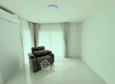 Spacious living room with modern armchair and large windows with curtains.