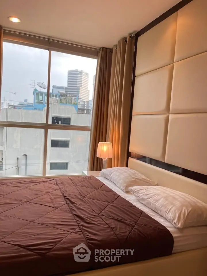 Modern bedroom with large window offering city view, featuring elegant decor and cozy ambiance.