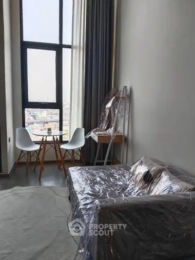 Modern living room with large window and city view, featuring a cozy seating area and stylish decor.