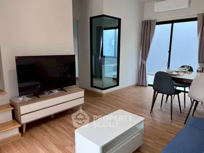 Modern living room with sleek furniture and dining area, featuring wooden flooring and large windows.