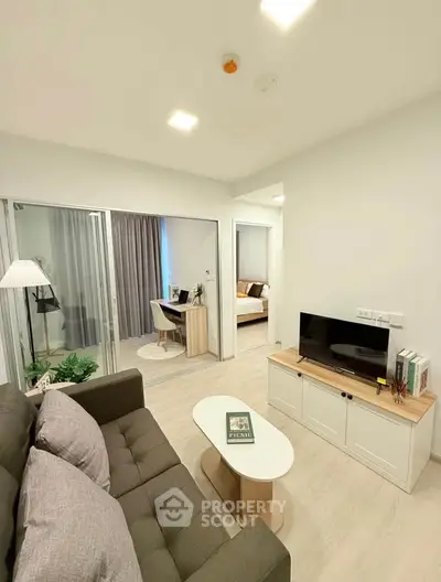 Modern living room with cozy sofa, TV unit, and view into bedroom and study area.