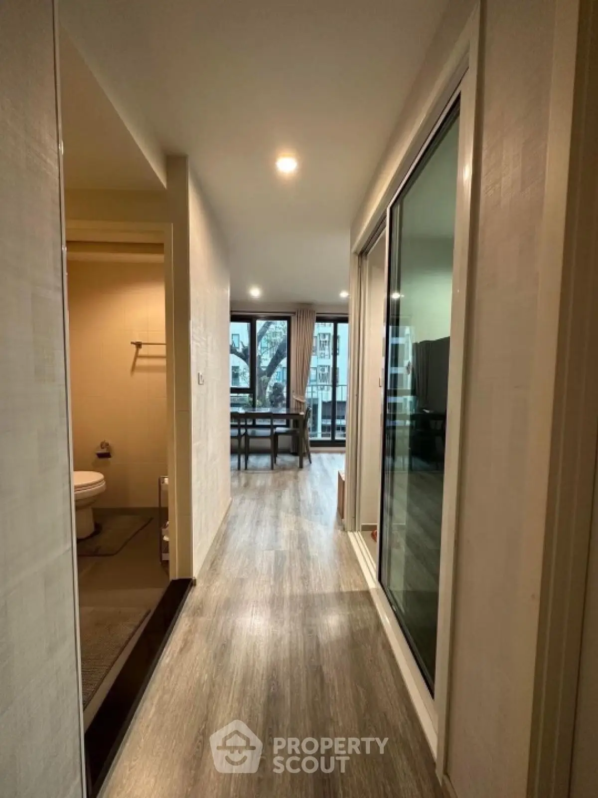 Modern apartment hallway with wooden flooring and glass sliding doors leading to a bright living area.