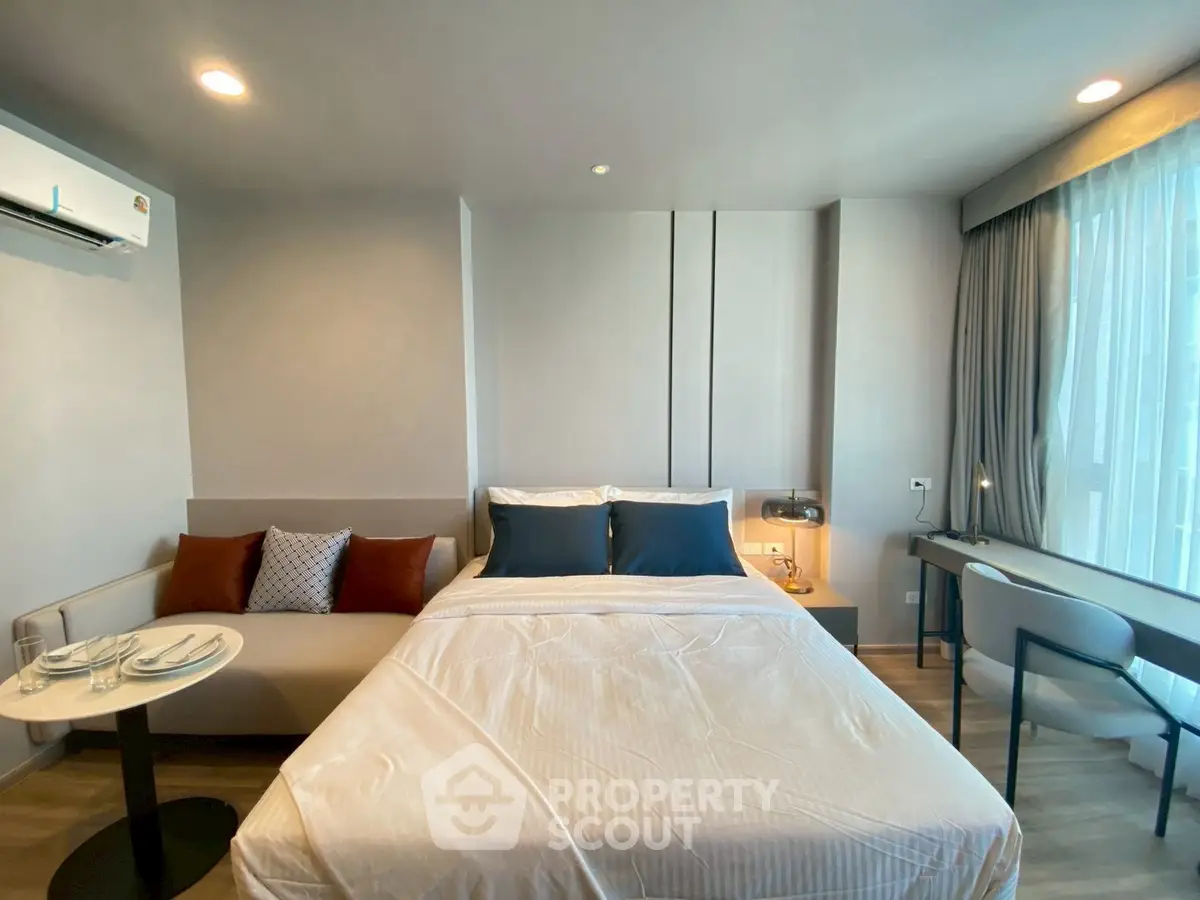 Modern bedroom with cozy seating area and large window in stylish apartment.