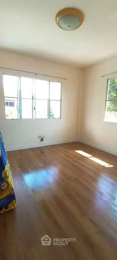 Spacious empty room with wooden flooring and large windows offering natural light.