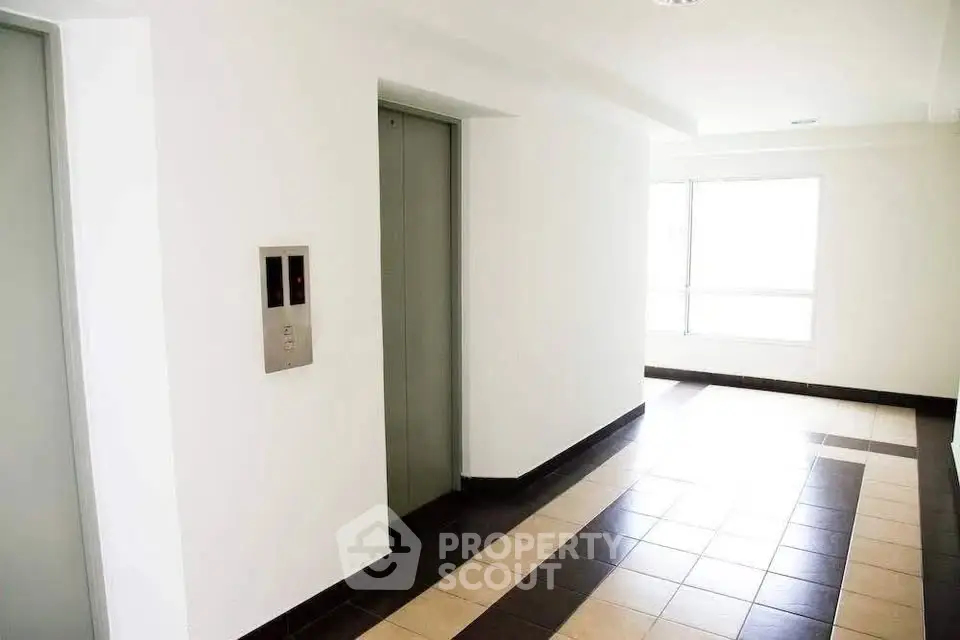 Bright modern building hallway with elevator access and tiled flooring.