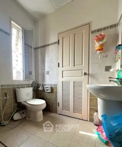 Bright bathroom with natural light, featuring a window, toilet, and sink in a tiled setting.
