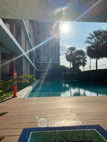 Luxurious poolside view with modern building and palm trees under bright sunlight.