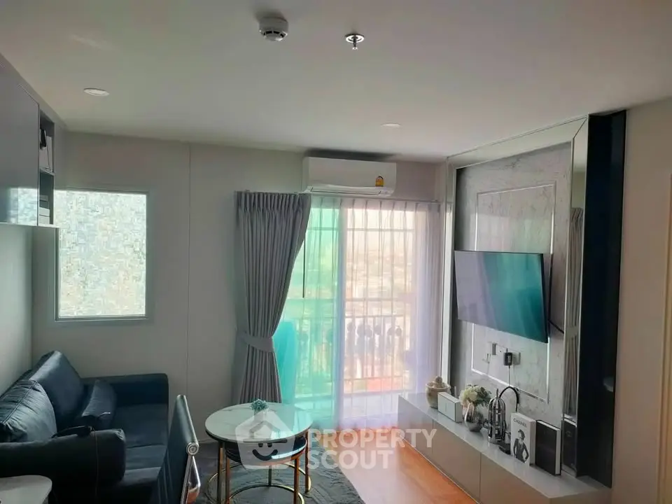 Modern living room with sleek design, featuring a wall-mounted TV, cozy seating, and natural light from large windows.