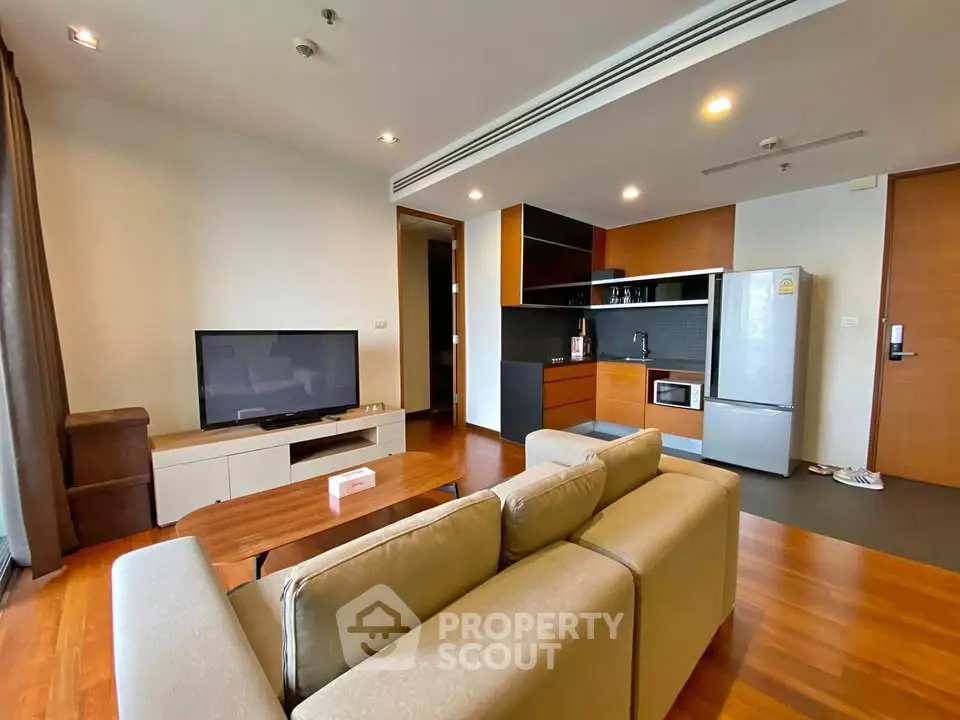 Modern living room with open kitchen, featuring sleek appliances and cozy seating area.