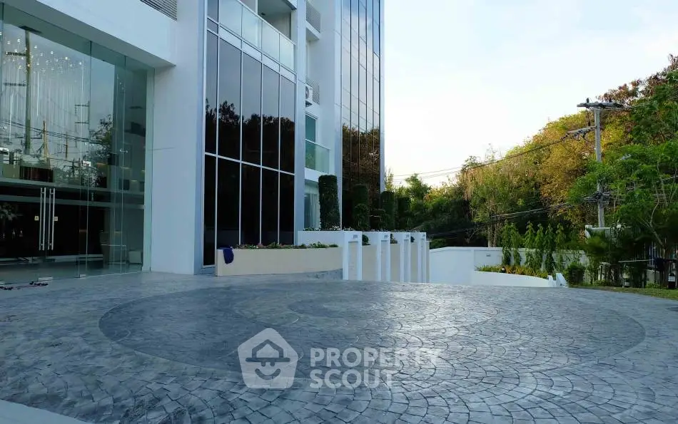 Modern building entrance with sleek glass facade and spacious circular driveway.