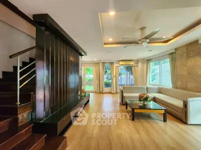Spacious living room with modern design and garden view, featuring elegant staircase and cozy seating area.