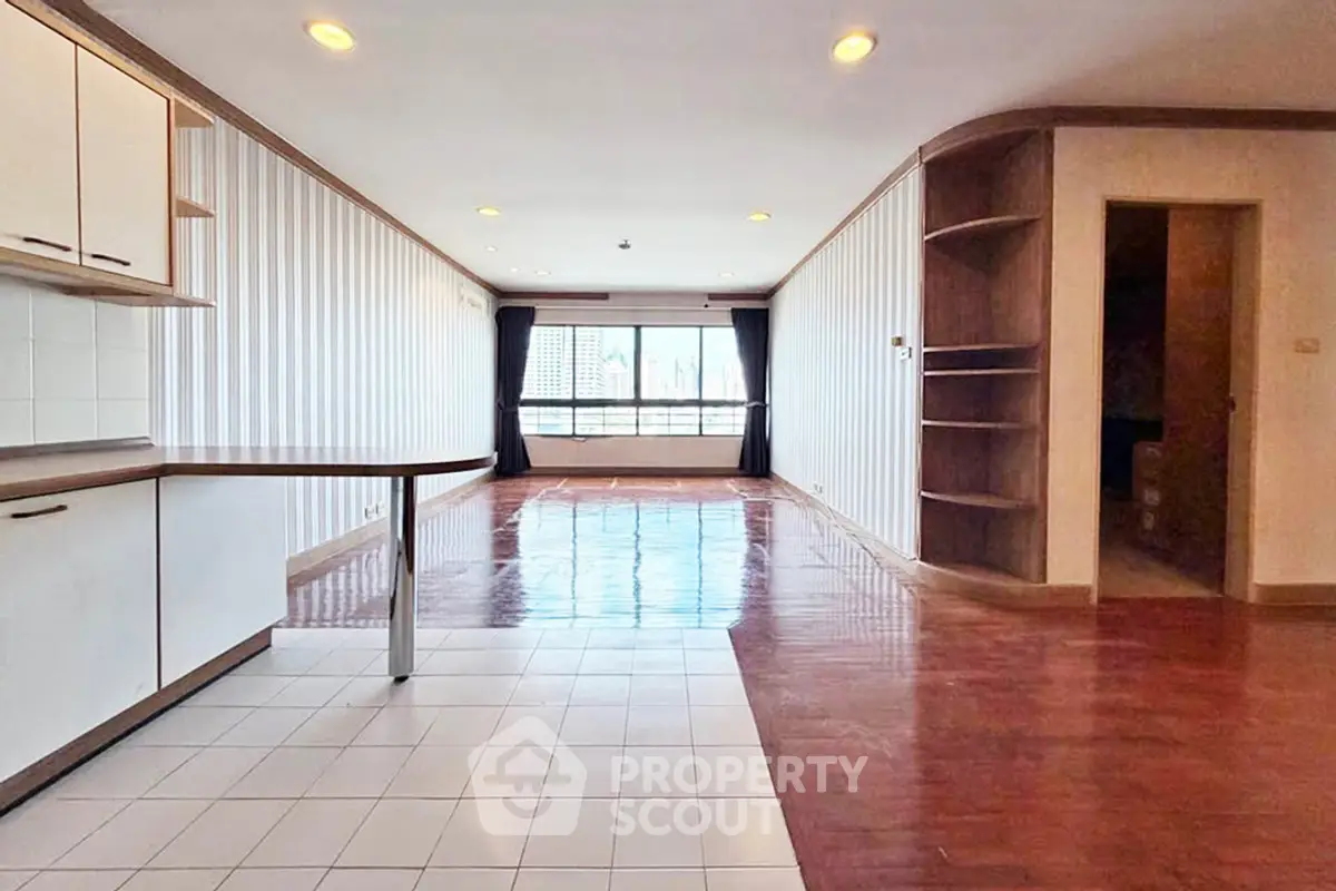 Spacious open-plan living room with wooden flooring and large windows offering natural light.