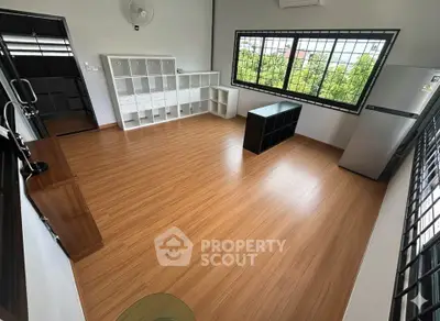 Spacious room with wooden flooring and large window offering a green view, featuring modern storage units and a fridge.
