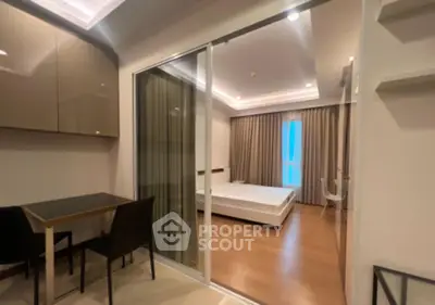 Modern apartment with sliding glass doors separating dining and bedroom areas, featuring sleek furniture and ambient lighting.