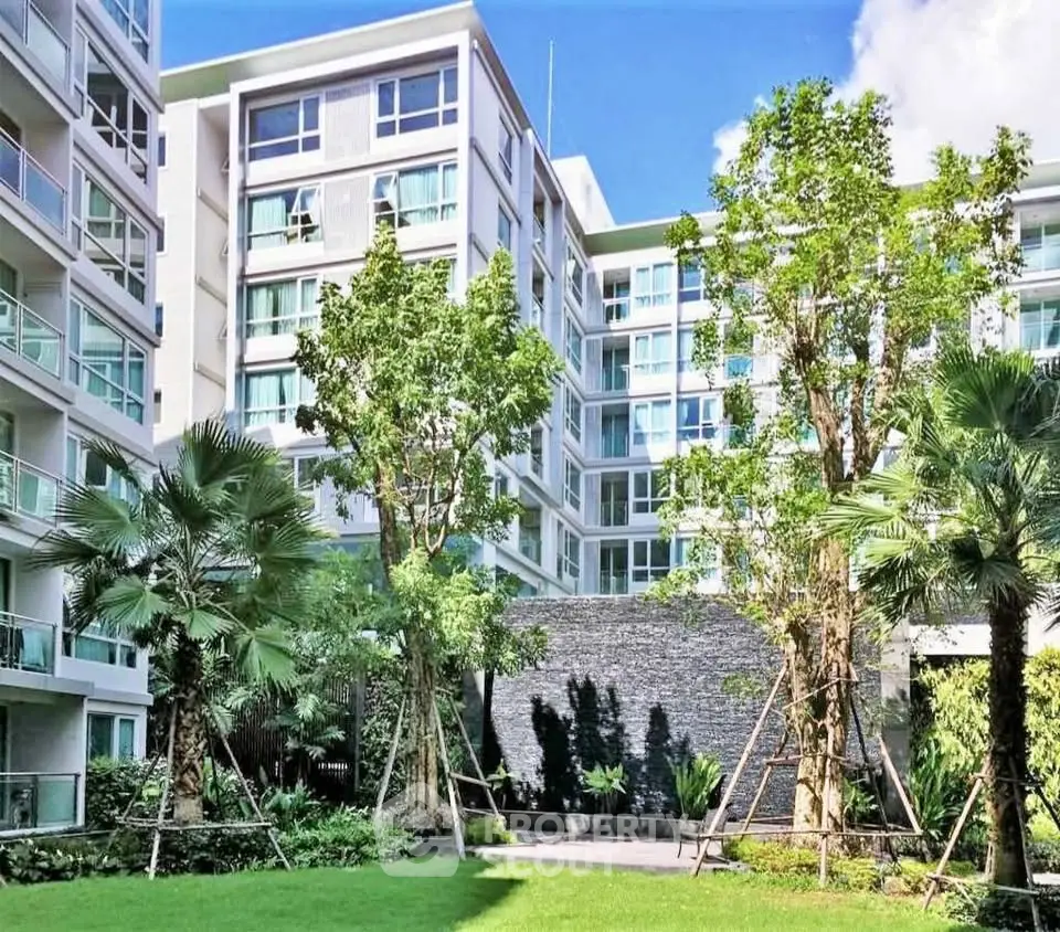 Modern apartment building with lush garden and tall trees, offering serene living environment.