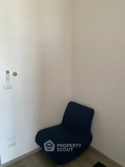 Minimalist corner with blue chair and wall-mounted remote in modern apartment.
