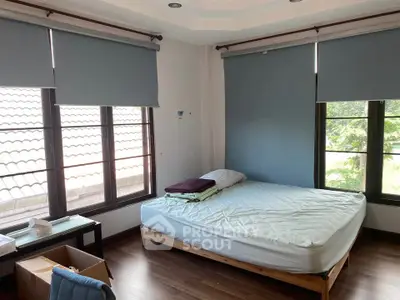 Spacious bedroom with large windows and natural light, featuring a comfortable bed and wooden flooring.
