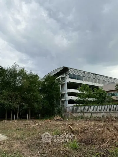 Modern building exterior with lush greenery and cloudy sky backdrop.