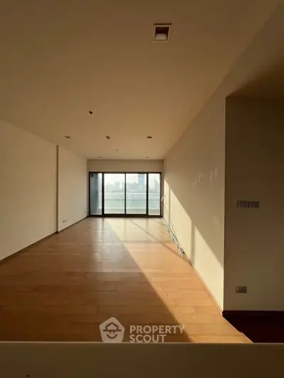 Spacious empty living room with wooden flooring and large windows offering city skyline view.