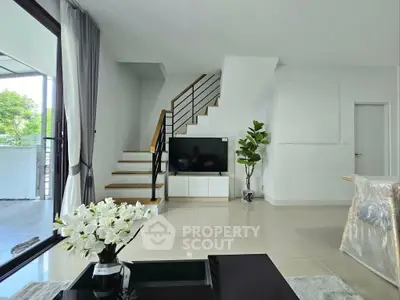 Modern living room with sleek staircase and large windows, offering a bright and airy atmosphere.